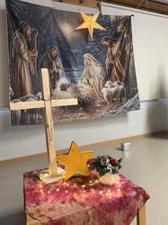 Ein christliches Kreuz vor dem Hintergrund eines Bildes, wo eine Krippe darauf zu sehen ist.